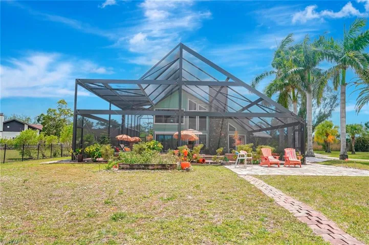 Back of property with glass enclosure, fence, a lawn, and a patio area