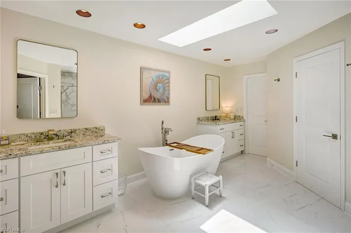 Bathroom featuring recessed lighting, a soaking tub, marble finish floor, a sink, and a skylight