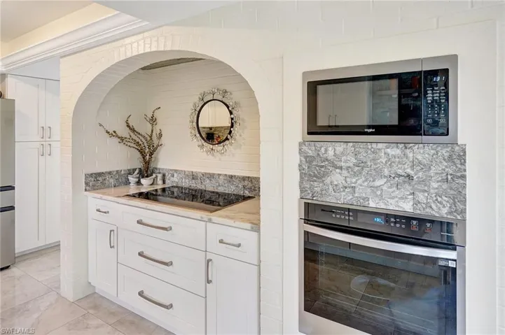 Kitchen with white cabinetry, light stone countertops, appliances with stainless steel finishes, and backsplash
