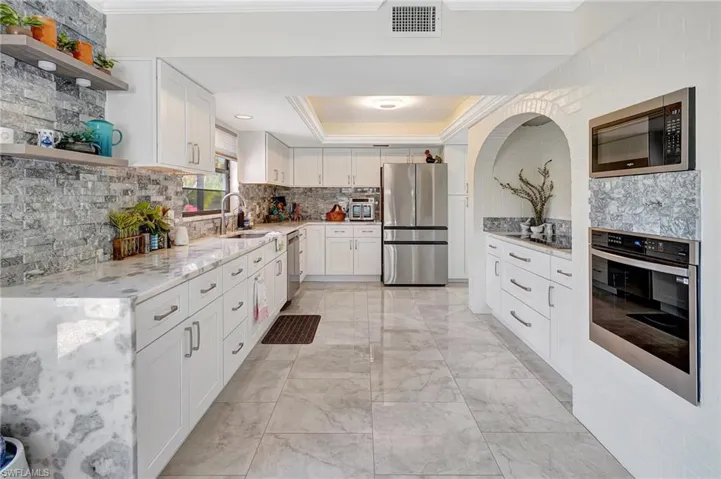 Kitchen with, appliances with stainless steel finishes, a sink, open shelves, and a tray ceiling