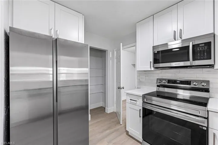 Kitchen featuring decorative backsplash, appliances with stainless steel finishes, light hardwood / wood-style floors, and white cabinetry