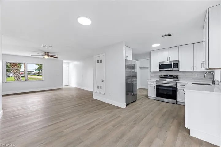 Kitchen featuring appliances with stainless steel finishes, sink, light hardwood / wood-style floors, white cabinetry, and ceiling fan