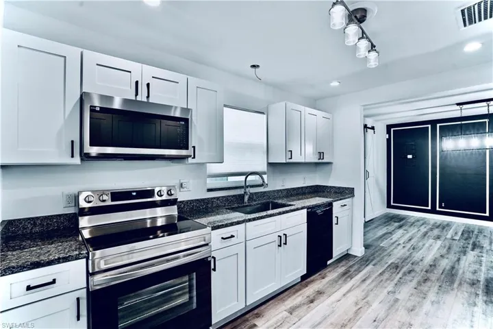 Kitchen with appliances with stainless steel finishes, white cabinets, light wood-style flooring, dark stone countertops, and recessed lighting
