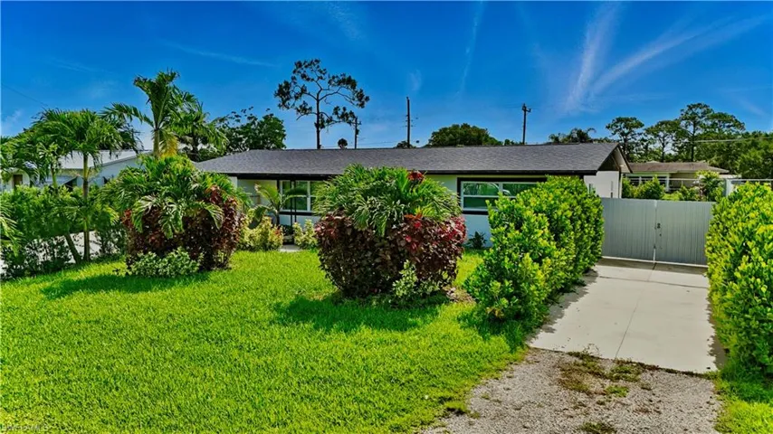 View of front of property featuring gravel driveway, a front lawn, and a gate