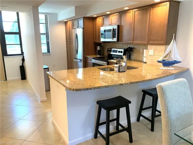 Kitchen featuring light stone counters, a kitchen bar, stainless steel appliances, a peninsula, and decorative backsplash