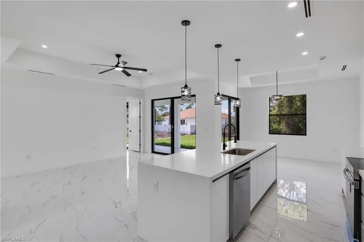Kitchen featuring a raised ceiling, plenty of natural light, a kitchen island with sink, light stone countertops, and light marble finish floors