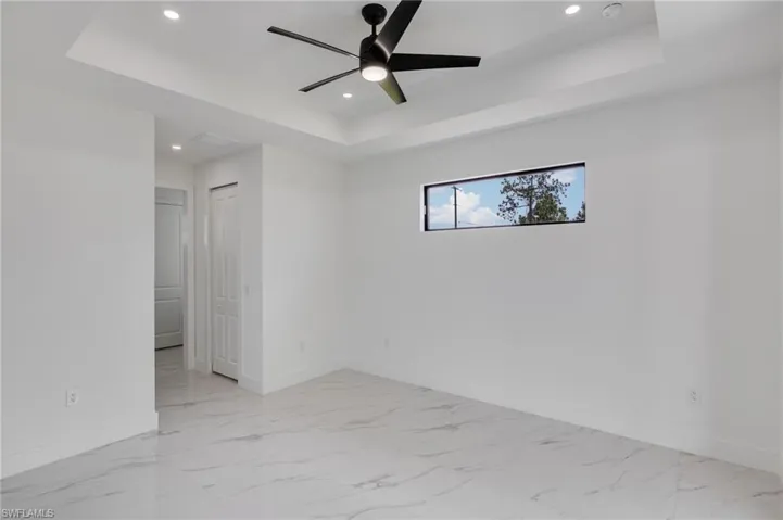 Unfurnished room featuring a tray ceiling, recessed lighting, ceiling fan, and light marble finish flooring