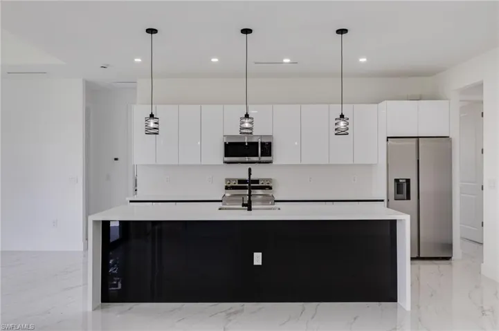 Dual tone kitchen featuring stainless steel appliances, light stone countertops, pendant lighting, an island with sink, and two tone cabinets