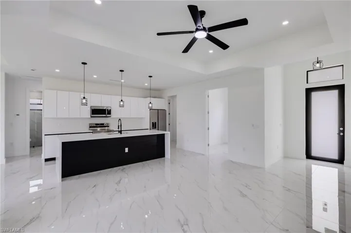 Two tone kitchen featuring open floor plan, an island with sink, hanging light fixtures, stainless steel appliances, and a tray ceiling