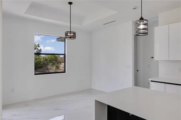 Unfurnished dining area featuring light marble finish flooring, a raised ceiling, and suspended lighting