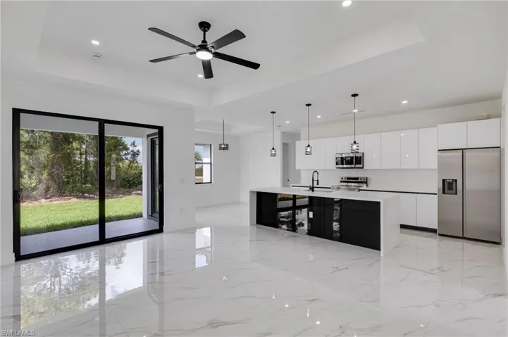 Kitchen with stainless steel appliances, a raised ceiling, a kitchen island with sink, white cabinets, and pendant lighting