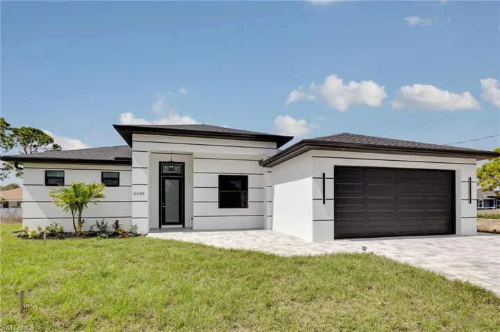 Prairie-style home featuring a front yard, decorative driveway, stucco siding, and a garage