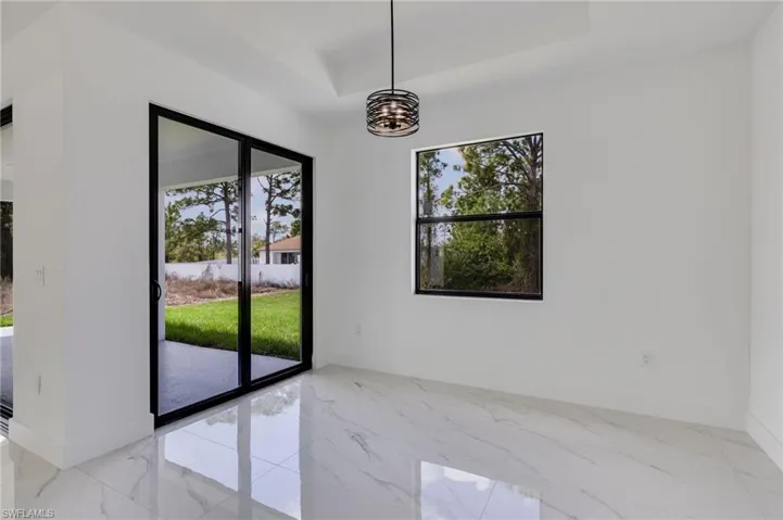 Unfurnished dining area featuring plenty of natural light, a raised ceiling, suspended lighting, and light marble finish flooring
