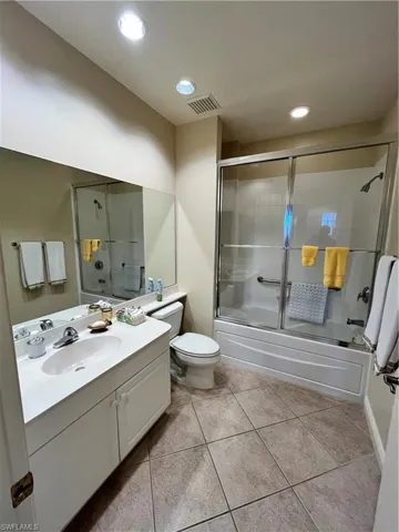 Full bathroom featuring combined bath / shower with glass door, vanity, toilet, and tile patterned flooring