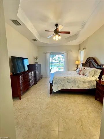 Bedroom featuring a raised ceiling, ceiling fan, slider to lanai, 2 walk in closets and crown molding
