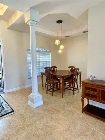 Dining room featuring a tray ceiling, decorative columns, and light tile patterned flooring