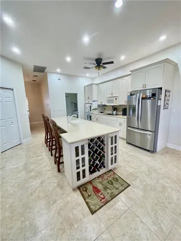 Kitchen featuring white appliances, a center island with sink, sink, ceiling fan, and a kitchen bar