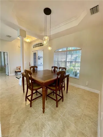 Dining area with crown molding, a raised ceiling, a notable chandelier, and ornate columns