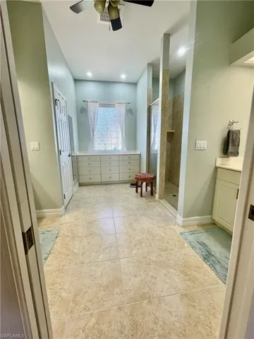 Bathroom with tile patterned floors, ceiling fan, vanity, and tiled shower