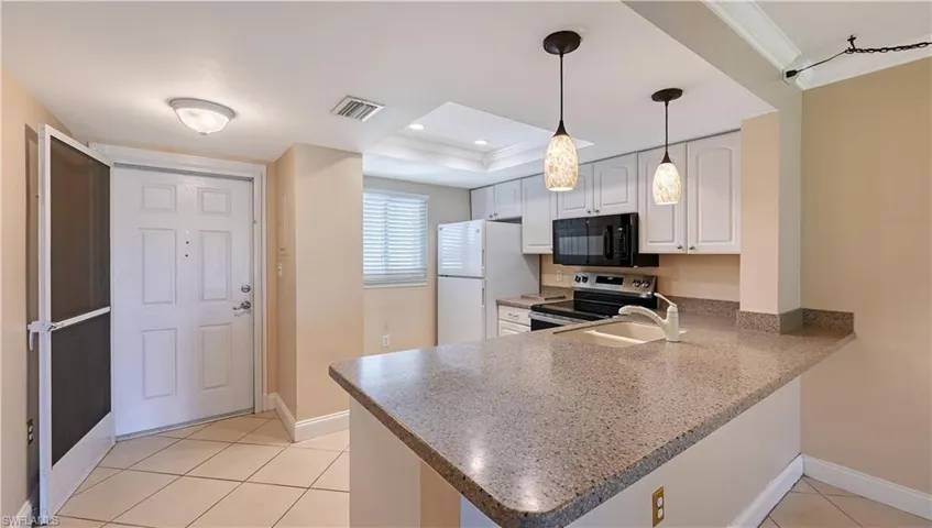 Kitchen with stainless steel electric stove, ornamental molding, freestanding refrigerator, light tile patterned floors, and black microwave