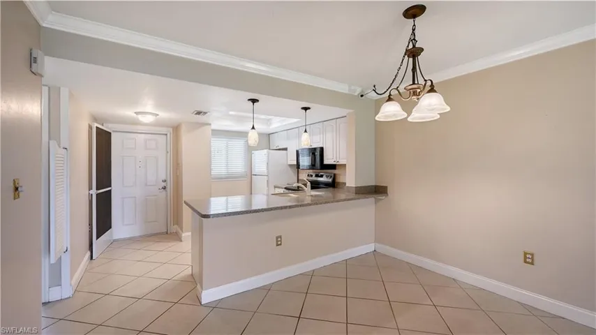 Kitchen featuring white cabinetry, a peninsula, decorative light fixtures, light tile patterned floors, and ornamental molding