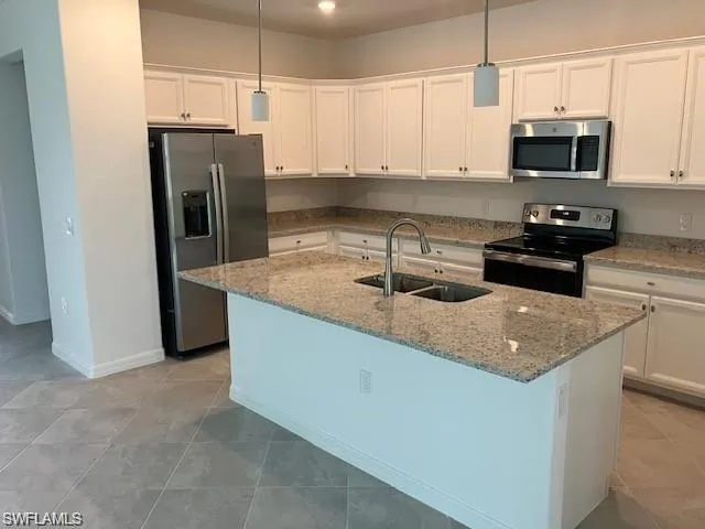 Kitchen featuring stainless steel appliances, white cabinets, an island with sink, light stone counters, and pendant lighting