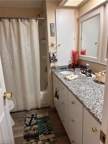 Full bathroom with hardwood / wood-style flooring, vanity, toilet, and shower / bath combo with shower curtain