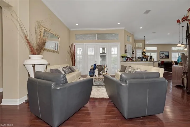 Living room with dark wood-style flooring, ornamental molding, healthy amount of natural light, and recessed lighting