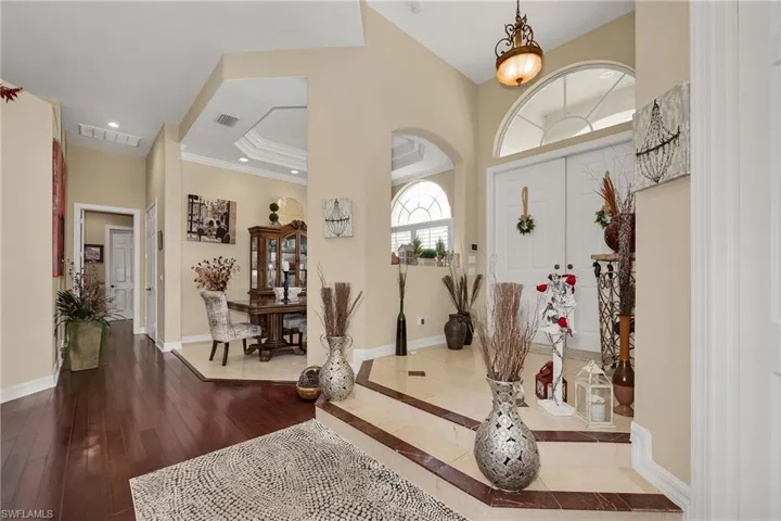 Foyer with dark wood finished floors, ornamental molding, arched walkways, a towering ceiling, and recessed lighting