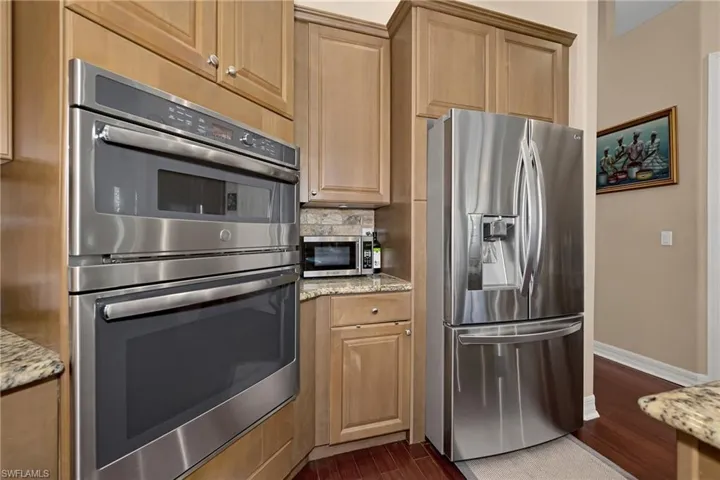 Kitchen featuring stainless steel appliances, dark wood finished floors, light stone countertops, and backsplash