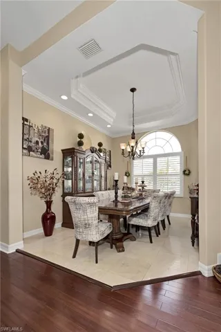 Dining room featuring light wood-type flooring, a raised ceiling, a chandelier, recessed lighting, and crown molding