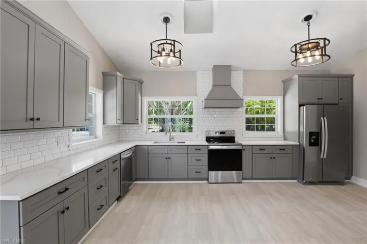 Kitchen featuring grey cabinetry, white countertops, stainless steel appliances, and two windows