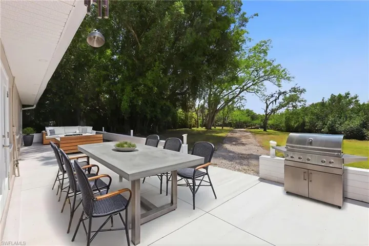 Virtually staged. Expansive outdoor patio featuring a dining area, a lounge area, and a built-in stainless steel grill, all overlooking a large green space