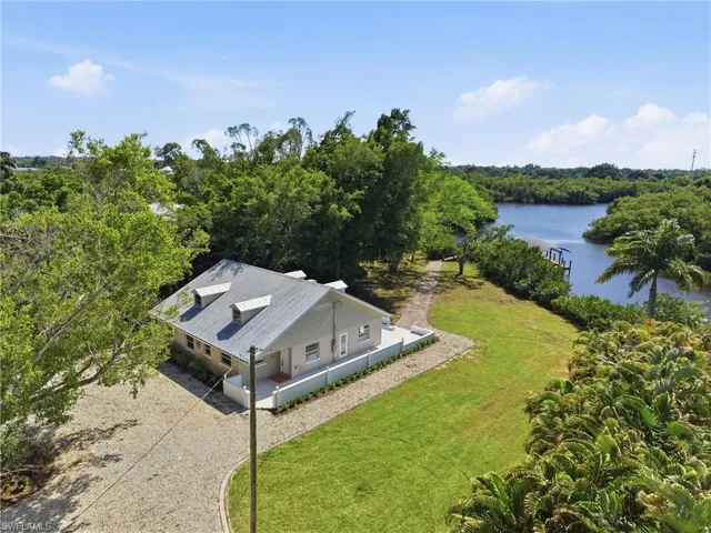 The property features a well-maintained lawn, a gravel driveway, and a dock extending into the waterway