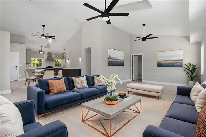 Virtually staged. The open concept living area features high vaulted ceilings with ceiling fans, light-colored flooring, and recessed lighting