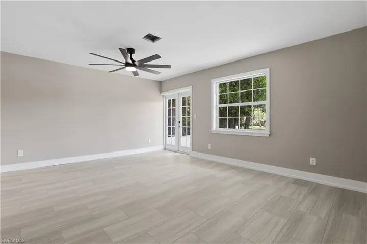 This spacious room features light-toned flooring, a ceiling fan with integrated lighting, and a large window providing views of greenery