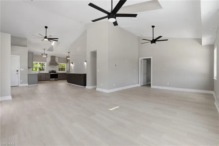 The spacious open-concept living area features light-toned flooring, vaulted ceilings with contemporary ceiling fans, and an inviting view into the kitchen