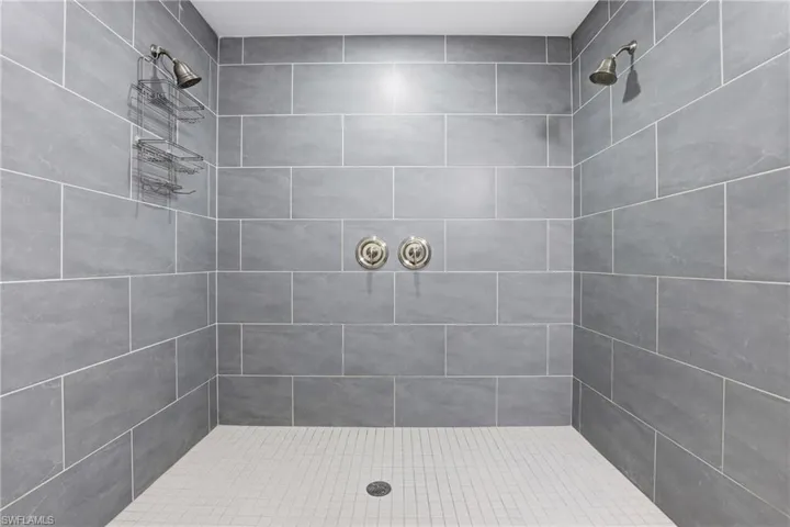 The shower features grey rectangular wall tiles, white square floor tiles, and dual shower heads