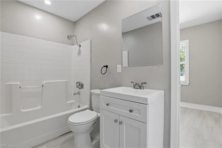 The bathroom features a white vanity with cabinet storage, a white toilet, and a white bathtub with a shower