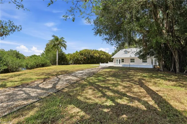 The property features a spacious yard with a gravel path, mature trees, and a distant view of water