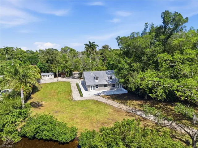 The property features a residence with a light-colored exterior and a gray roof, surrounded by extensive green landscaping including mature trees and a lawn
