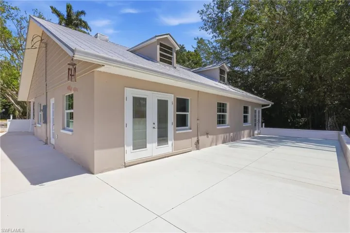 The property features a light-colored stucco exterior with white trim, a gray metal roof, and dormer windows