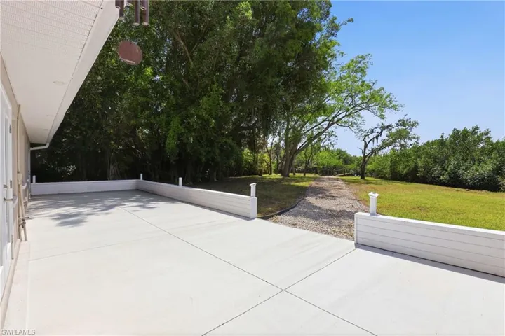 Expansive concrete patio with white privacy walls, offering views of the surrounding natural landscape with mature trees and a grassy area