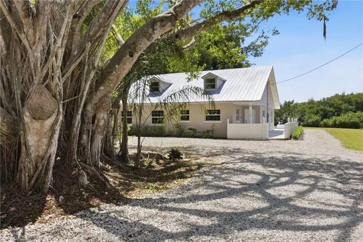 The property features a gravel driveway, a light-colored exterior, and a metal roof