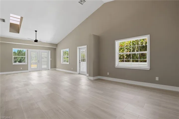 Spacious living area featuring light-colored tile flooring, vaulted ceilings, and skylights