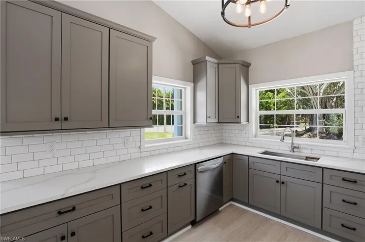 Kitchen featuring grey cabinetry, white countertops, white subway tile backsplash, and a stainless steel dishwasher