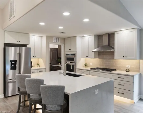 Kitchen featuring sink, appliances with stainless steel finishes, wall chimney exhaust hood, and tasteful backsplash