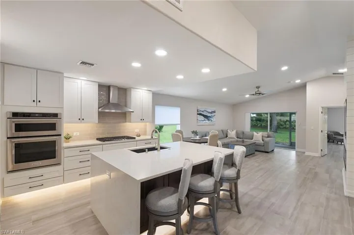 Kitchen with sink, stainless steel double oven, wall chimney range hood, gas stovetop, and vaulted ceiling