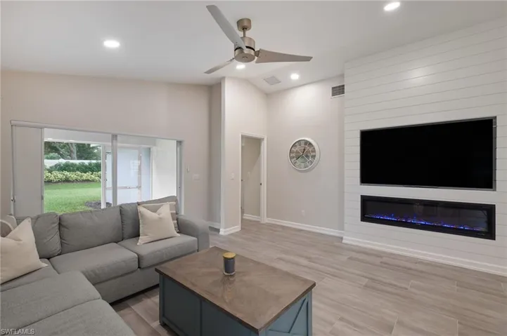 Living room featuring ceiling fan, high vaulted ceiling, light hardwood / wood-style flooring, and a large fireplace