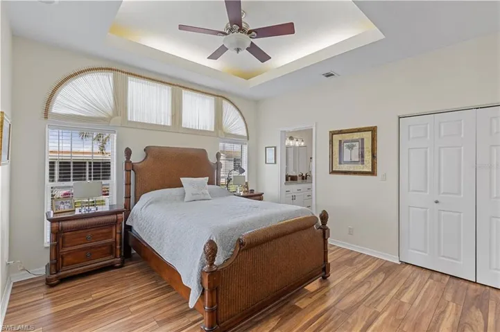 Bedroom with ceiling fan, wood finished floors, connected bathroom, a closet, and a raised ceiling